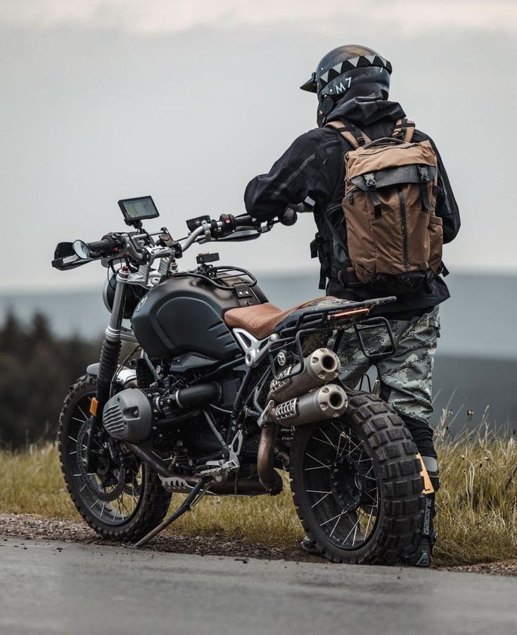 a man with a back pack on standing next to a motorcycle