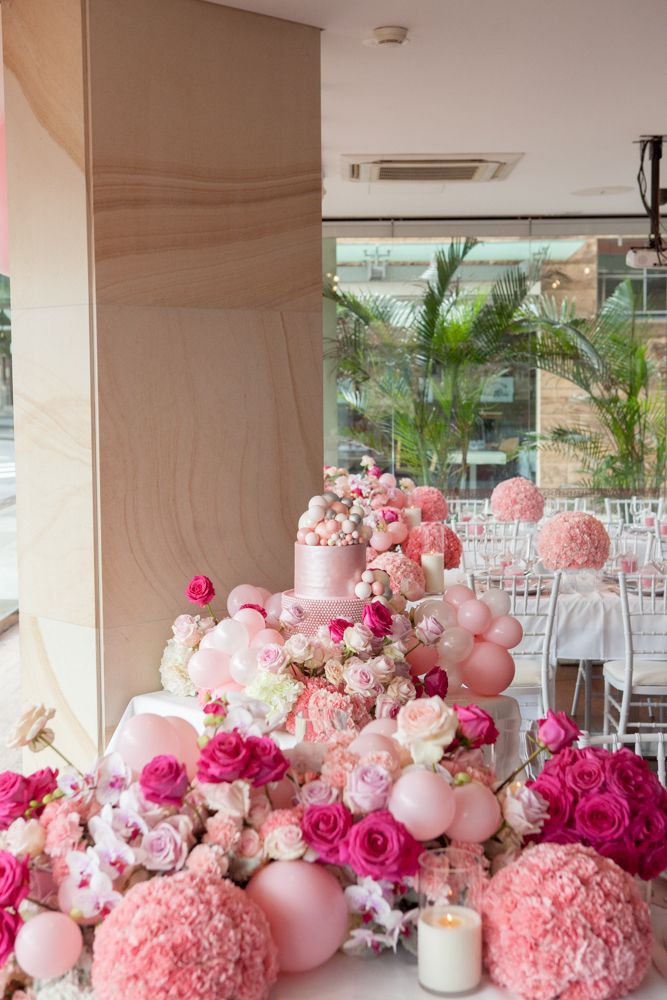 a table topped with pink and white flowers next to a tall cake covered in balloons