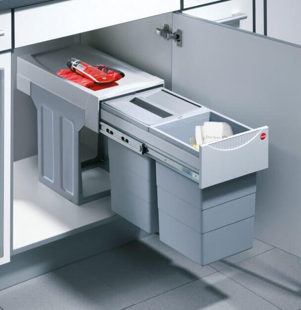 an open drawer in the middle of a kitchen with two trash cans and a dustbin