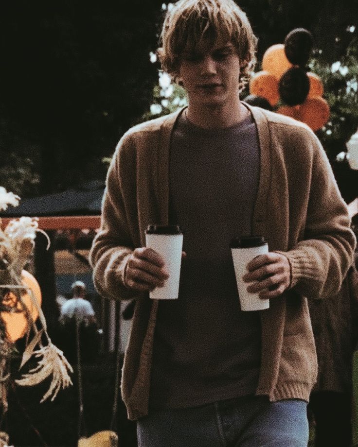 a young man holding two coffee cups while standing in front of an outdoor area with balloons