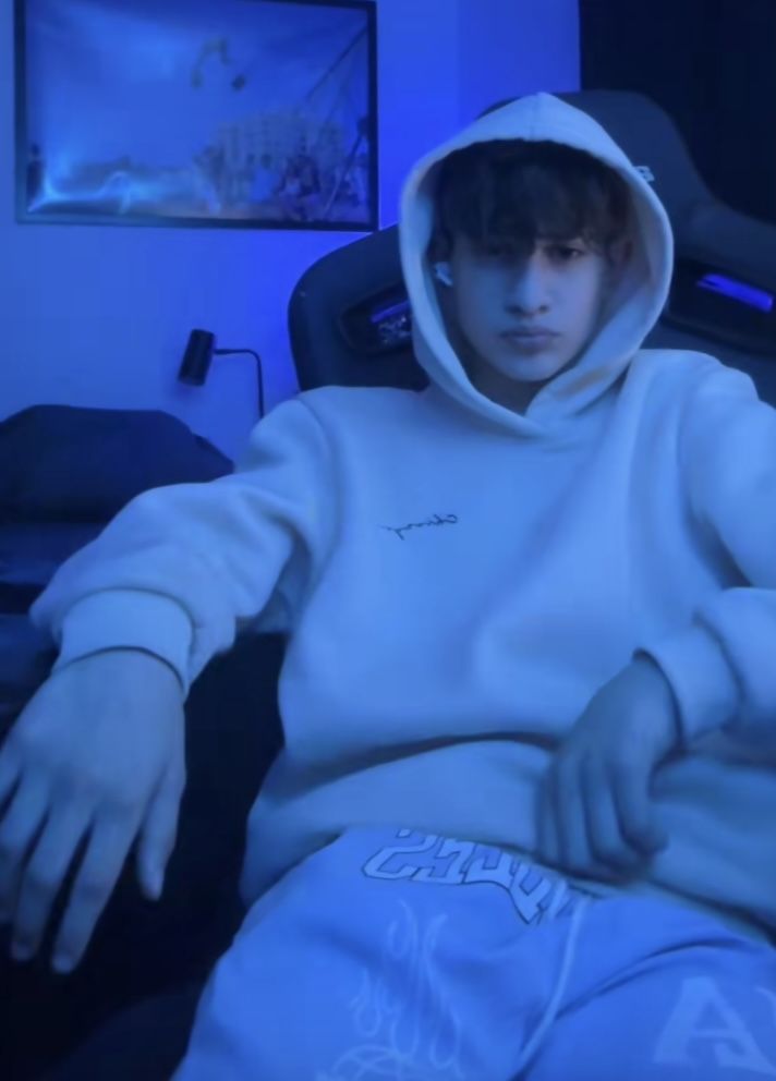 a boy in a white hoodie sitting on a couch with his hands out to the side