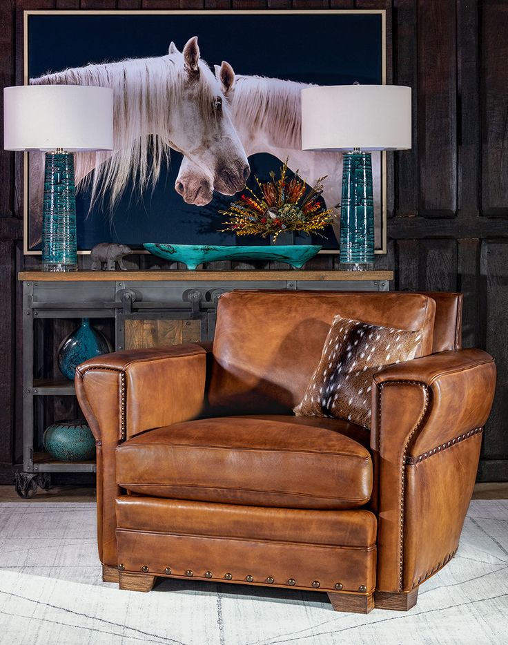 a brown leather chair sitting in front of a painting on the wall next to a lamp