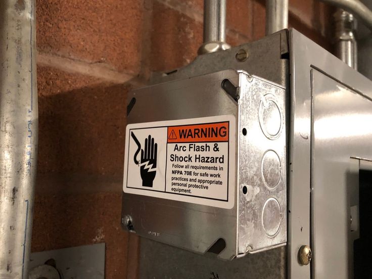 a warning sign is posted on the side of a metal box in front of a brick wall