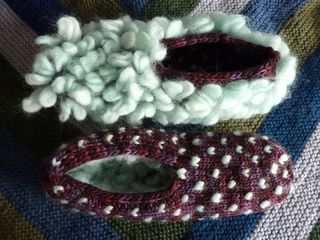 two knitted slippers are sitting on a striped blanket, one is white and the other is red