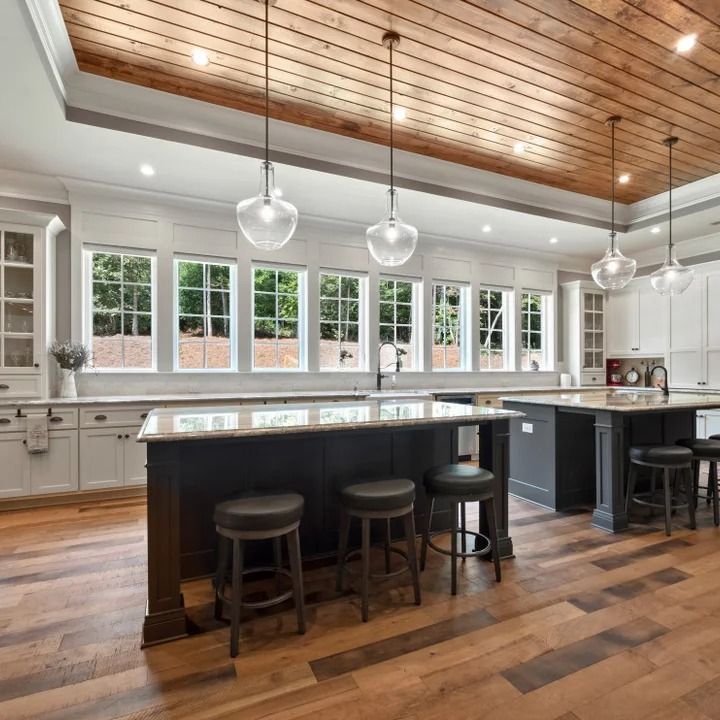 a large kitchen with an island and bar stools in the center, surrounded by wooden flooring