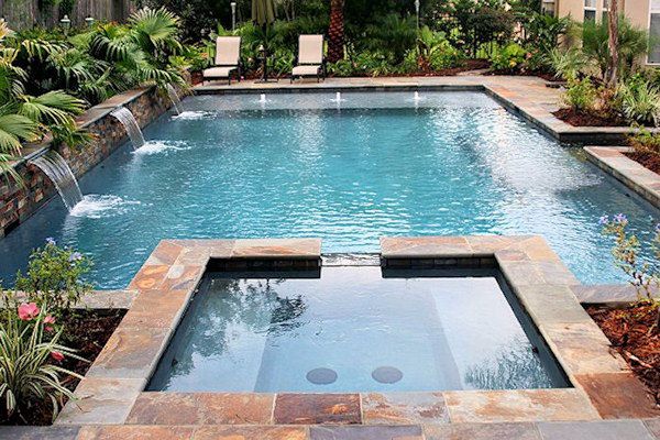 a small pool with a waterfall in the middle surrounded by greenery and trees, along with lounge chairs