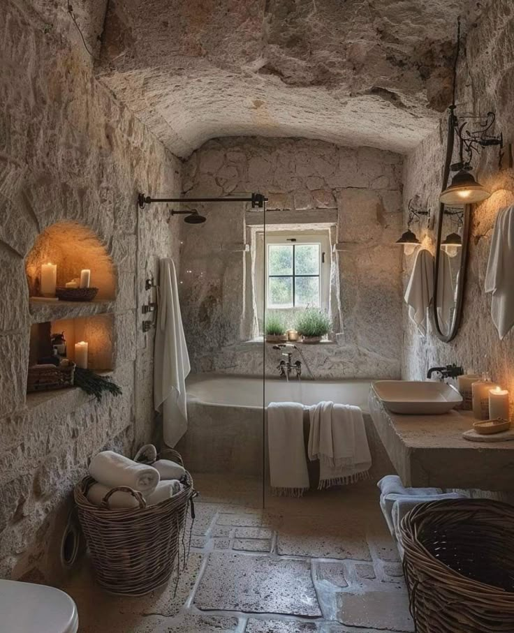 a bathroom with stone walls and flooring has candles on the wall next to the tub