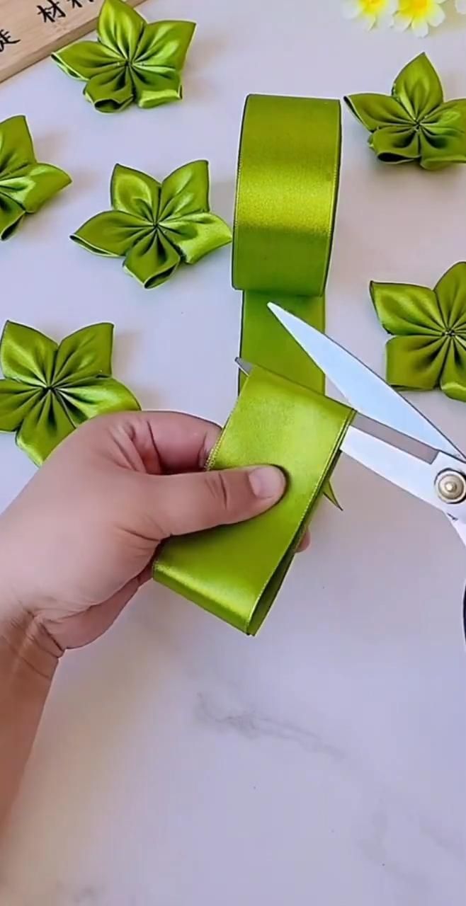 someone cutting green ribbon with scissors on top of a white table covered in paper flowers