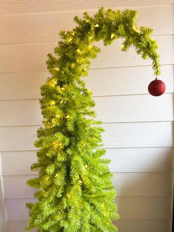 a tall green christmas tree next to a white house with an ornament hanging from it's side