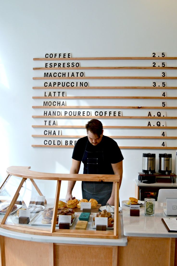 a man standing at a counter in front of a coffee shop with writing on the wall behind him