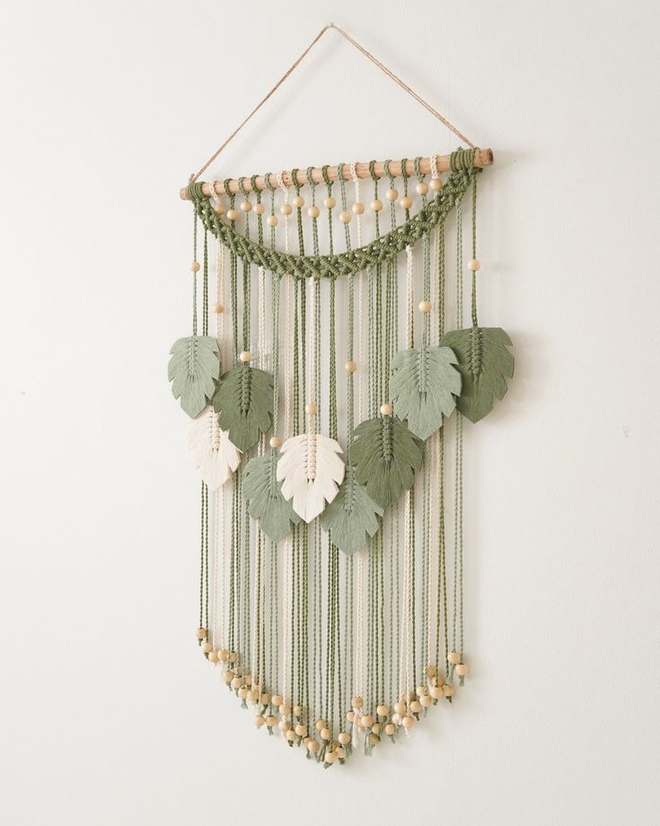 a green and white wall hanging with beads, leaves and shells on it's sides