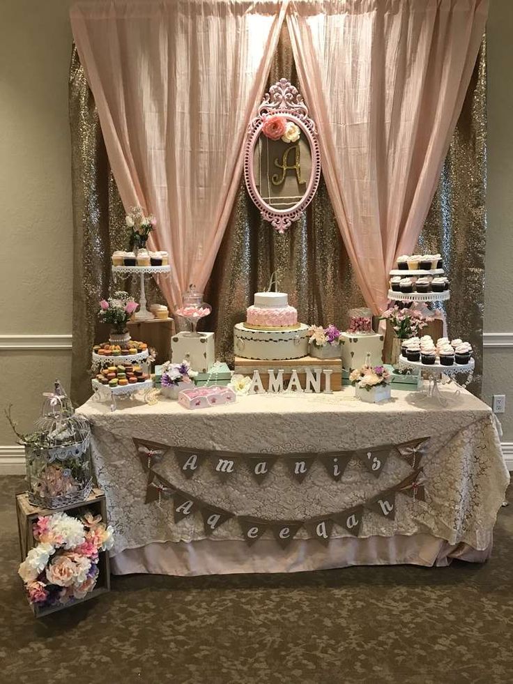 a table topped with cakes and cupcakes under a window covered in pink curtains