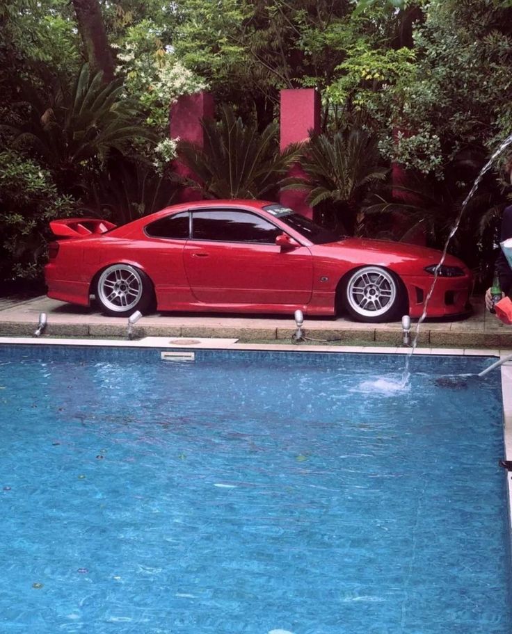 a red sports car parked next to a swimming pool in the middle of a garden