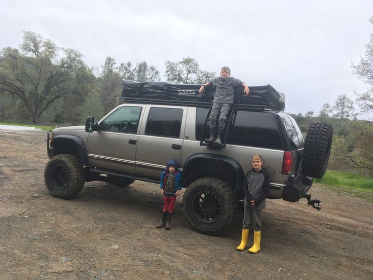 two people standing on the back of a truck with an suv in the middle of it