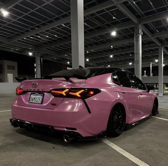 a pink sports car parked in a parking lot with its hood up and tail lights on