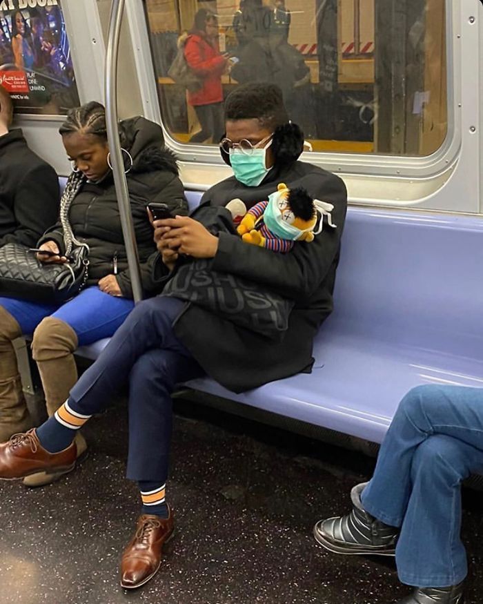 two people sitting on a subway looking at their cell phones while wearing facemasks