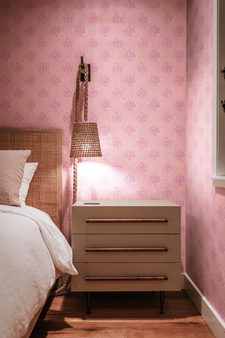 a bedroom with pink wallpaper and a white dresser next to a bed in the corner