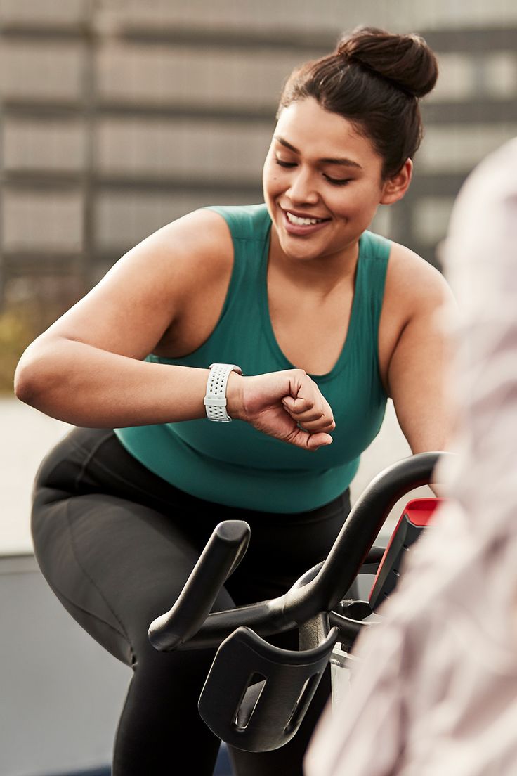 a woman smiles as she rides an exercise bike with her hand on the handlebars