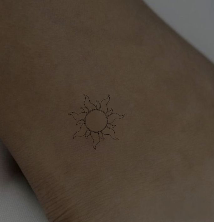 a small sun tattoo on the left side of the arm is shown in black ink