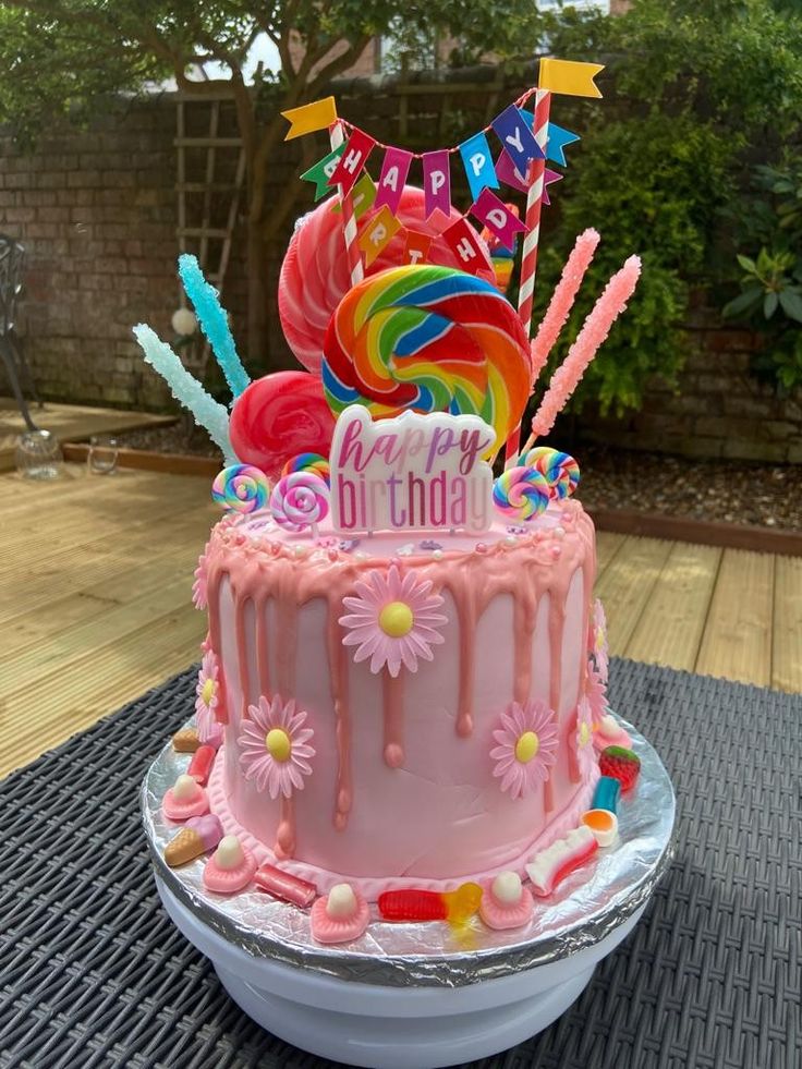 a pink birthday cake sitting on top of a metal pan covered in icing and decorations