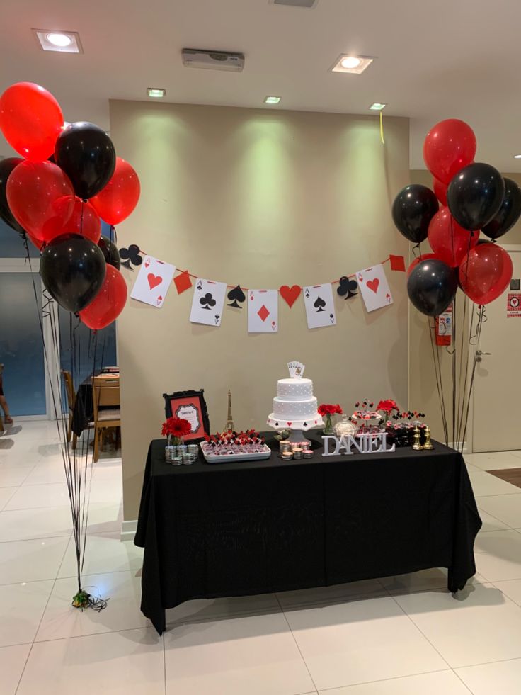 a table topped with lots of red and black balloons next to a cake on top of a table