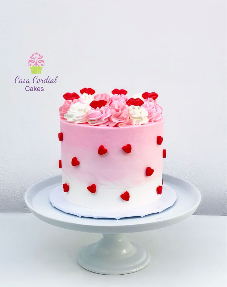 a pink and white cake with red hearts on the top is sitting on a plate