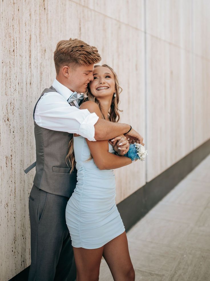 a young man and woman embracing each other in front of a wall with their arms around each other