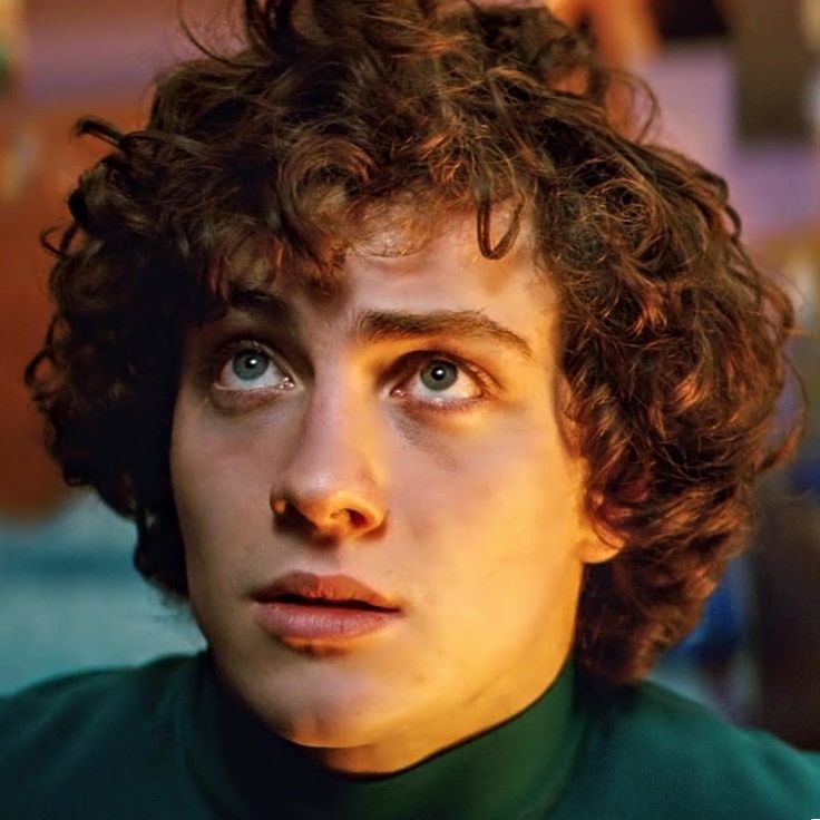 a close up of a person with curly hair and green shirt looking at the camera