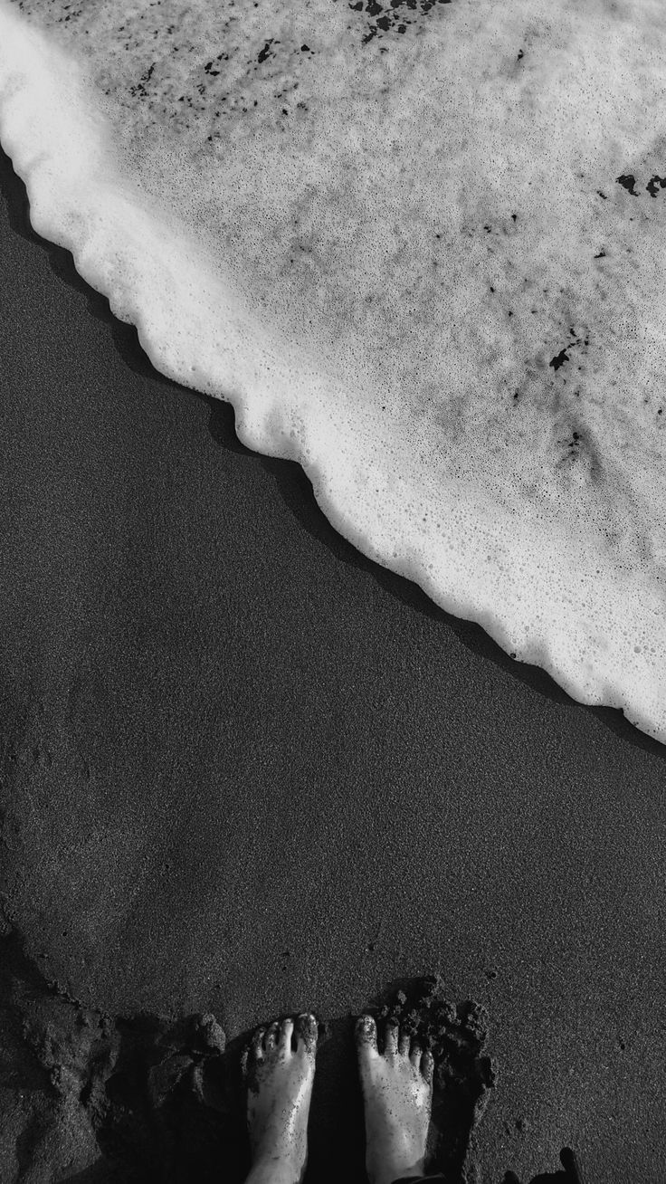 someone is standing on the beach with their feet in the sand near the ocean water