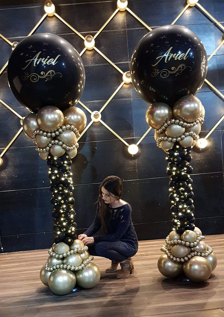 a woman kneeling down next to two tall black and gold balloons with name on them