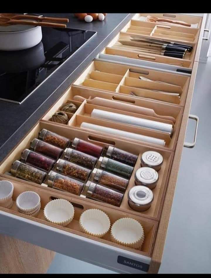 an open drawer filled with lots of different items on top of a counter next to bowls and utensils