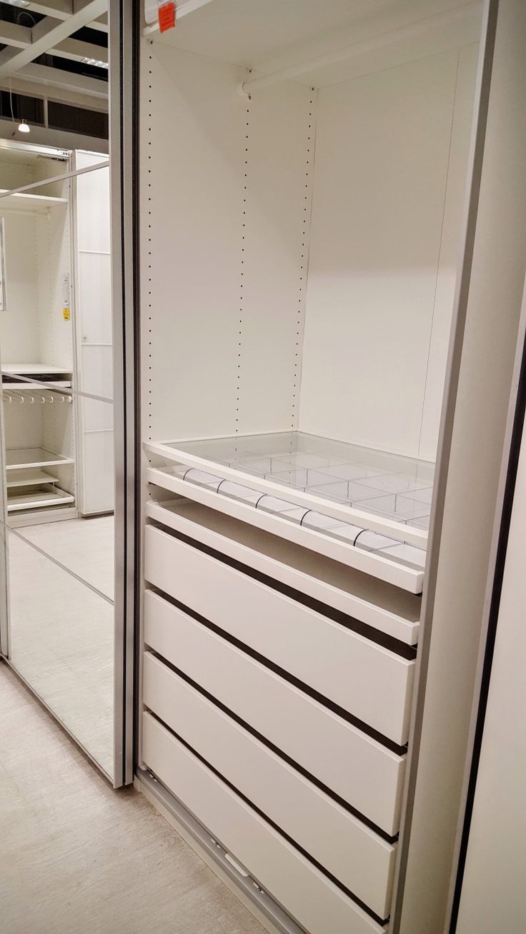 an empty storage room with white cabinets and drawers on the wall, in front of a mirror