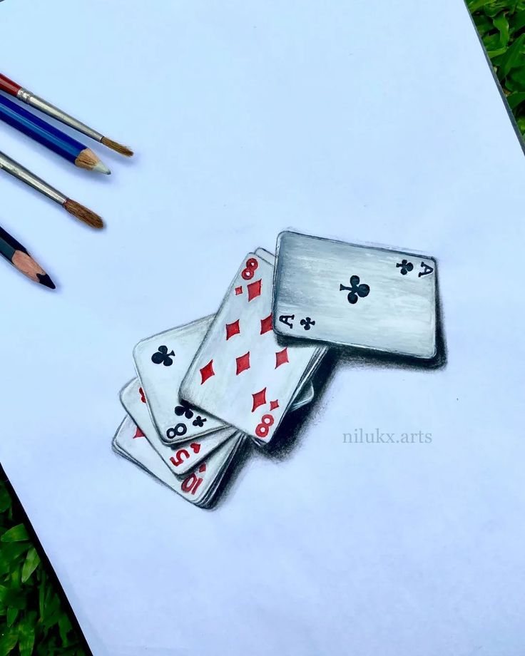 three playing cards are sitting on top of a piece of paper with colored pencils next to them