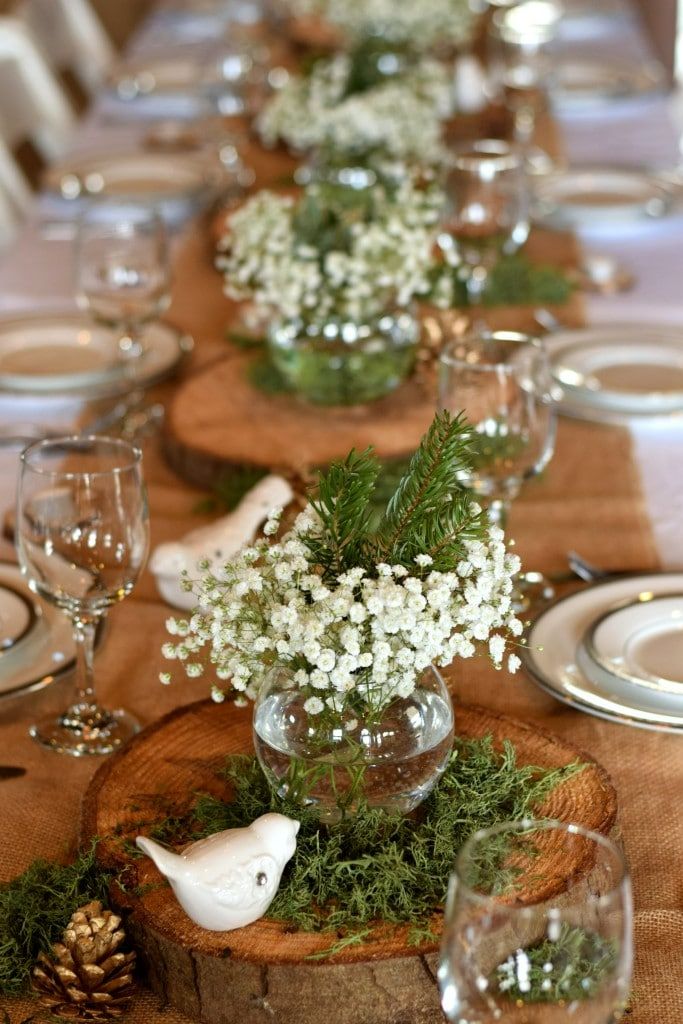 the table is set with white flowers and greenery in glass vases on wood slices