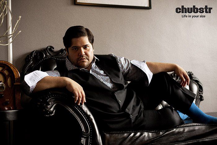 a man sitting on top of a black chair next to a wall with a clock