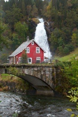 a red house sitting on the side of a river next to a bridge and waterfall