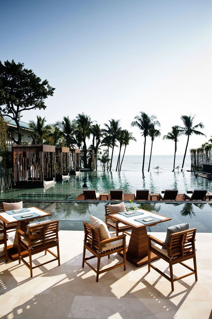 an outdoor dining area with tables and chairs next to the pool in front of palm trees