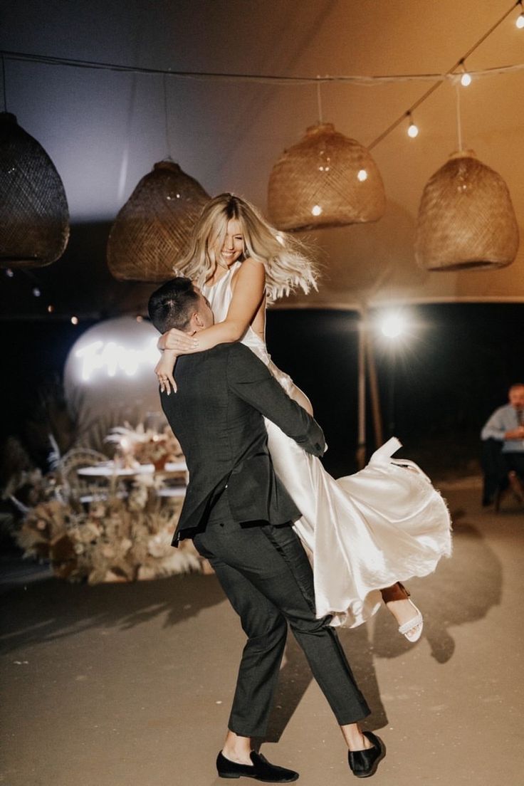 a man and woman are dancing together in the middle of a room with lights hanging from the ceiling