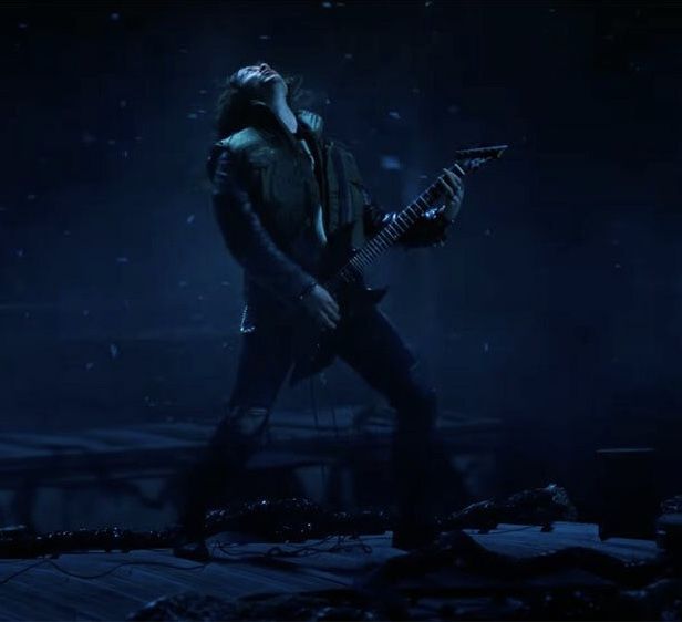 a man playing an electric guitar on stage in the dark with snow falling all around him