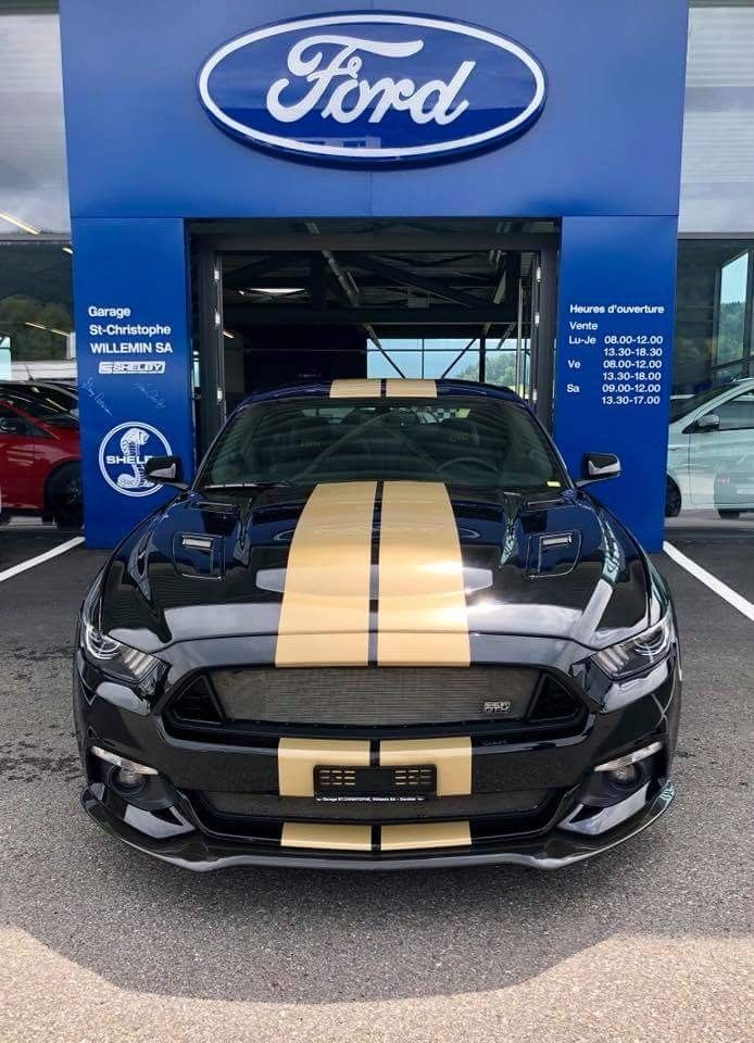 a black and gold mustang parked in front of a ford dealership with the word ford on it