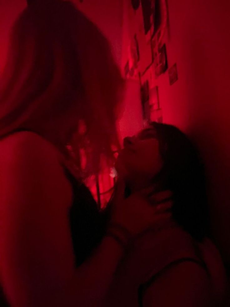 a woman is in the dark with red light on her face and arm, while she has her eyes closed