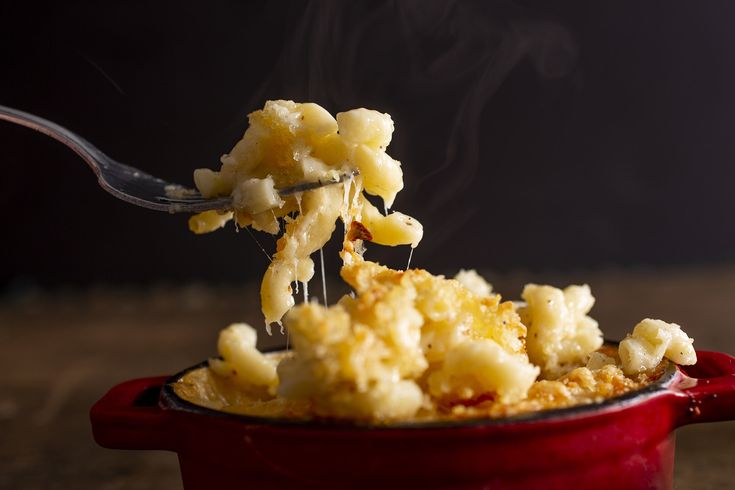 a red bowl filled with macaroni and cheese being lifted from the pot by a fork