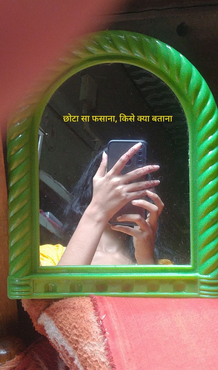 a woman taking a selfie with her cell phone in front of a green mirror