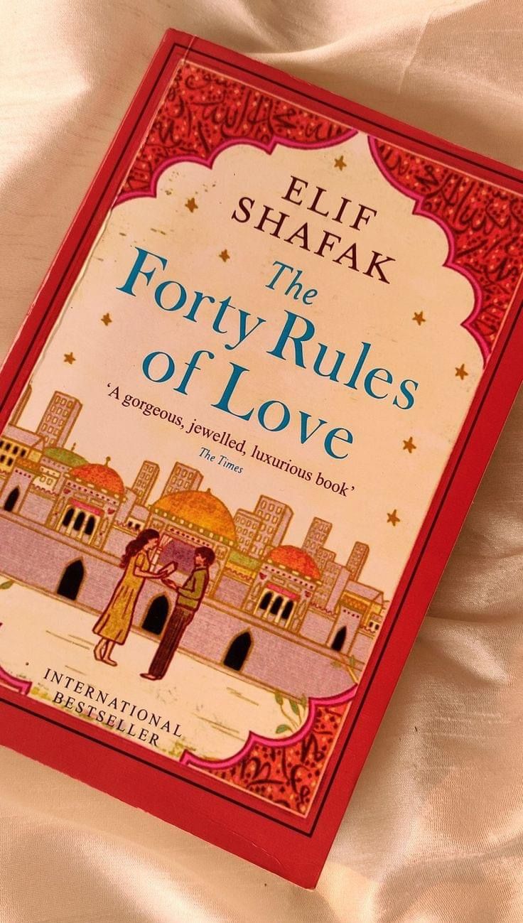 the forty rules of love by eli shafak on a white bed sheet with red trim