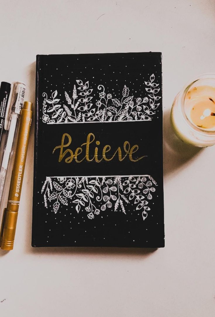 a notebook with the word believe written on it next to some pens and a cup of coffee