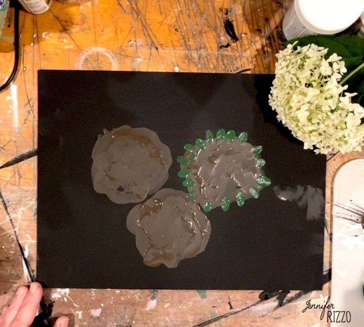 a person is painting flowers on a piece of black paper with brown and green paint