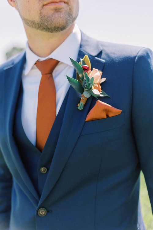 a man wearing a blue suit with an orange tie and flower boutonniere