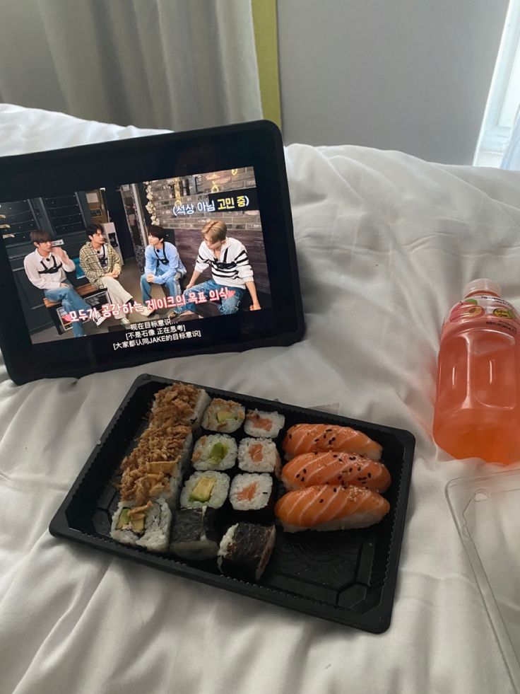 a tray with sushi and drinks on a bed