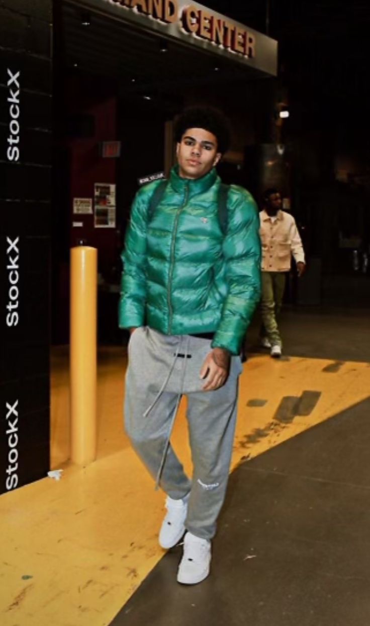 a man standing in front of a sign wearing a green jacket and grey sweatpants