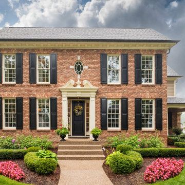 a large brick house with black shutters on the front and side windows, surrounded by landscaping